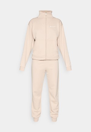 Beige träningsdräkt i set bestående av en zip-up jacka med hög krage och matchande byxor med elastiska muddar. Tillverkad av mjukt, strukturerat tyg.