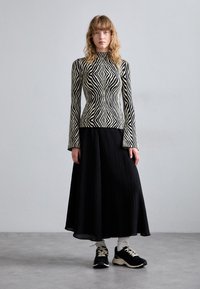 Haut à manches longues rayé noir et blanc associé à une jupe plissée noire et des baskets noires. Texture douce, haut ajusté et jupe fluide.