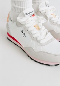 Hvide sneakers med grå ruskindsaccenter, lyserøde og røde detaljer samt hvide snørebånd. Har et mærketikett på tungen. Sort gummisål.