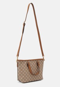 Sac fourre-tout beige avec motif de feuilles, anses en cuir et bandoulière ajustable, accents en métal doré, forme rectangulaire et fermeture éclair sur le dessus.