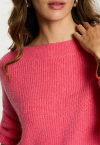 Maglione rosa a maglia con scollo ampio e texture a coste. Il tessuto morbido cade sulle spalle, mostrando una vestibilità rilassata e un colore ricco.