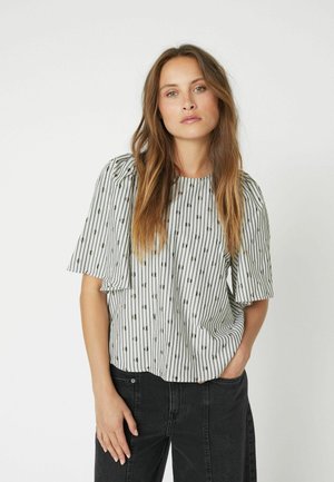 Blouse rayée blanche avec des manches courtes évasées et de petits pois noirs. Coupe décontractée, tissu doux, avec un col haut et des volants subtils.