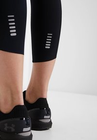 Černé sportovní legíny s reflexními stříbrnými akcenty na lýtkách, doplněné černými lehkými běžeckými botami se síťovaným svrškem.