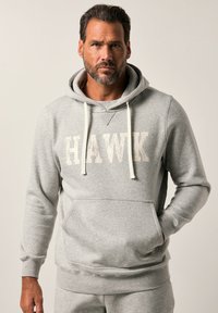 Felpa grigia in misto cotone con tasca frontale, cordini bianchi e la scritta "HAWK" in grandi lettere stampate sul petto. Tessuto morbido.