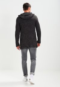 Ciemnoszary, dzianinowy kardigan z kapturem, z długimi rękawami i bocznymi rozcięciami, noszony na jasnoszare dżinsy i białe sneakersy. Prosty i teksturowany design.