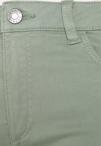 Vaaleanvihreä farkkukangas, jossa on sileä pinta, metallinen nappi, ommellut saumat ja vyölenkki.