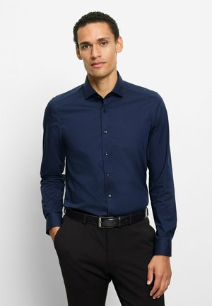 Marineblaues Hemd mit langen Ärmeln, spitzem Kragen und glatter Textur, kombiniert mit schwarzen Hosen und einem Gürtel.