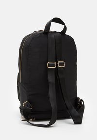 Svart tygryggsäck med justerbara axelremmar, detaljer i guld vid dragkedjan och ett handtag på toppen, mot en enkel vit bakgrund.