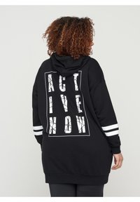 Felpa nera con cappuccio dal taglio lungo, con grafica bianca "ACT LIVE NOW" e strisce bianche sui maniche. Materiale morbido.