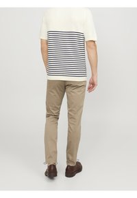 Korte mouwen, crèmekleurig gebreid shirt met marineblauwe horizontale strepen op de achterkant; gecombineerd met lichtbruine chino's en bruine veterschoenen.