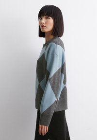 Grauer und hellblauer Pullover im Argyle-Muster mit Rundhalsausschnitt und langen Ärmeln, gefertigt aus einem weichen, strukturierten Strickmaterial.
