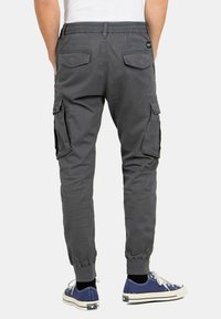 Pantalones cargo grises con puños elásticos, que cuentan con bolsillos laterales y traseros. Están hechos de una tela duradera, diseñada para la comodidad y la practicidad.