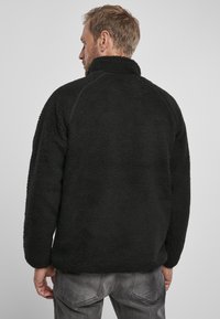 Pullover in pile nero con colletto alto, superficie texturizzata e vestibilità comoda. Presenta maniche lunghe e orlo dritto. Dettagli di cucitura visibili.