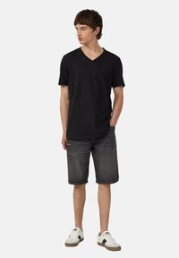Zwarte v-hals t-shirt van zachte stof, gecombineerd met donkere denimshorts en witte sneakers met grijze accenten. Casual en ontspannen pasvorm.