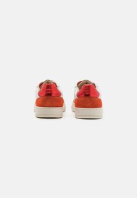 Par med sneakers med en hvit læroverdel, røde metalliske og oransje suede detaljer, og en strukturert gummisåle.