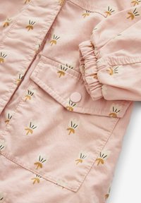 Veste en coton rose avec un motif floral, dotée de poignets élastiques, d'une poche à rabat et d'une fermeture par bouton. Texture douce avec des détails décoratifs.