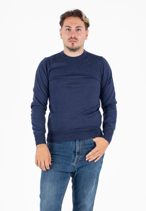 Maglione a maniche lunghe di colore blu navy, realizzato in tessuto a maglia, con scollatura rotonda e orlo a coste. Il modello lo indossa con jeans di denim.