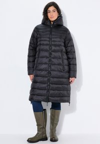 Abrigo acolchado negro con cierre frontal, cuello alto y mangas largas. Cuenta con un diseño acolchado, bolsillos laterales y llega hasta la mitad de la pantorrilla.