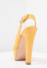 Žlutý semišový elegantní sandal s vysokým podpatkem, zaoblenou špičkou a přezkovým popruhem. Obsahuje platformu a strukturovaný povrch.