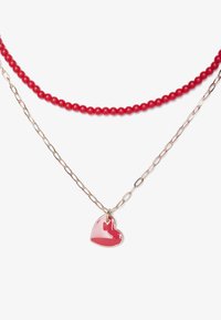 Collar de cuentas rojas combinado con una cadena dorada, que presenta un colgante en forma de corazón rojo brillante. La textura suave y los materiales variados generan un interés visual.