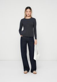 Haut à manches longues gris foncé avec un ourlet en peplum, associé à un jean en denim foncé à coupe ample. Sac blanc décontracté avec des accents perforés.