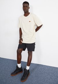 Beige oversized t-shirt with a small multicolored logo, black cargo shorts, and black high-top sneakers with gum soles.