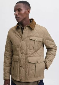 Chaqueta exterior acolchada color beige con cuello de pana, bolsillos frontales y botones a presión, que presenta un diseño texturizado y acolchado.
