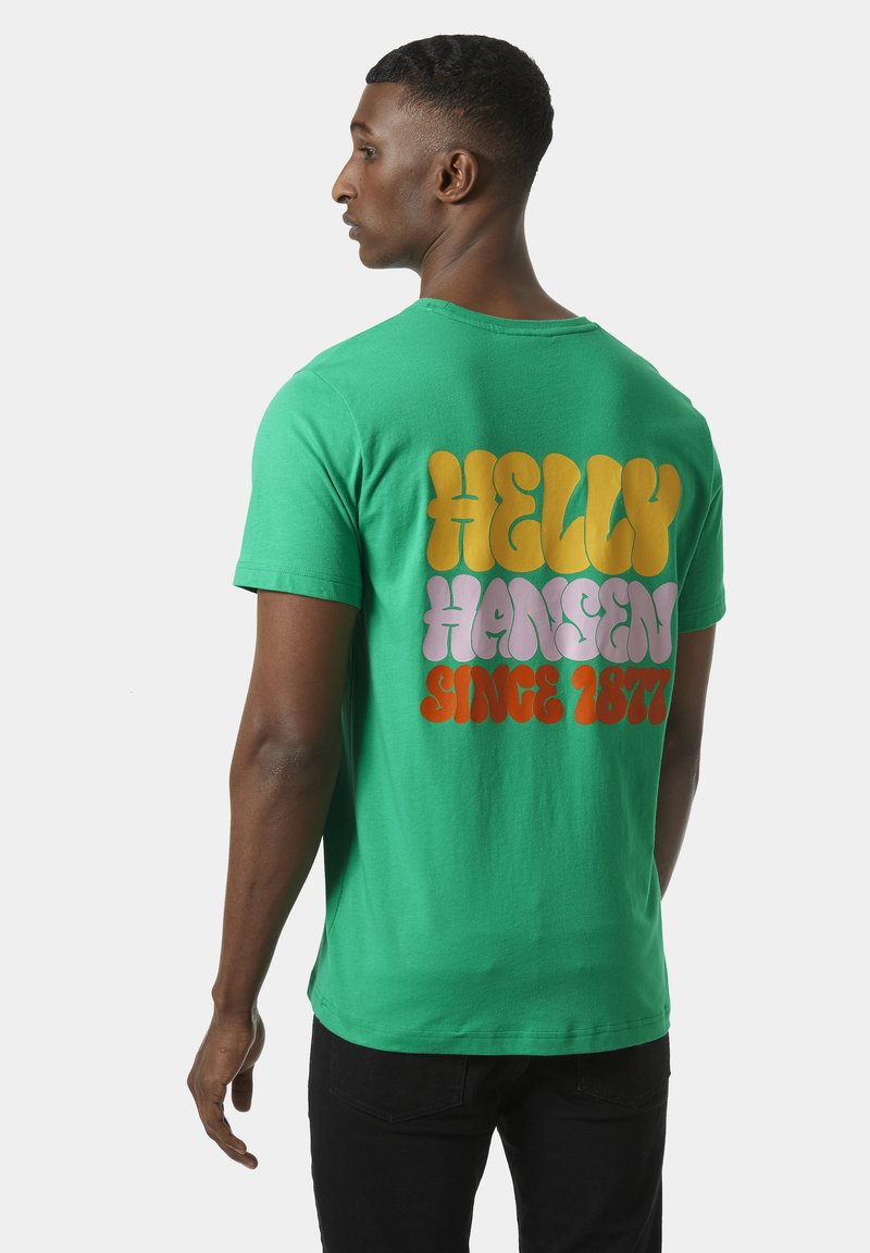 Zelené bavlněné tričko s velkým vícebarevným nápisem na zadní straně, který zní "HELly HANSEN SINCE 1877." Krátké rukávy a uvolněný střih.