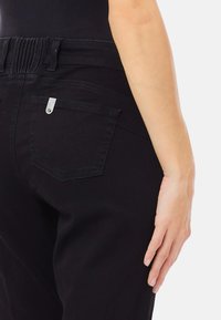 Črne jeans hlače z visokim pasom z nabranim detajlom, subtilnim šivom in majhnim srebrnim okrasjem na zadnjem žepu.