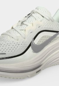 Λευκό παπούτσι Nike για τρέξιμο με επάνω μέρος από δίχτυ, ασημένιο λογότυπο Swoosh, κορδόνια και μαλακή σόλα με το κείμενο "CUSHION" στην πλευρά.