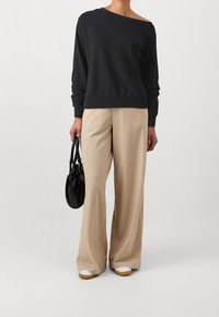 Felpa nera senza spalle, pantaloni beige a gamba larga e una piccola borsa nera. Sneakers bianche con suola in gomma. Vestibilità semplice e rilassata.