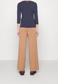 Maglietta a maniche lunghe blu navy con scollatura ampia, abbinata a pantaloni beige a gamba larga, caratterizzati da una texture morbida e linee pulite e semplici.