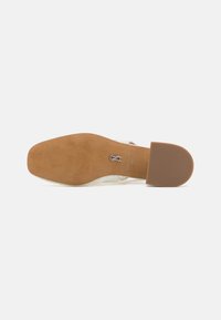 Sandale avec une semelle en caoutchouc beige, dessus transparent avec un motif texturé et un petit talon large. Présente un détail de logo en relief sur la semelle intérieure.