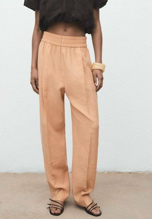 Pantalones sueltos de color melocotón con cintura elástica, hechos de tela ligera. Sandalias negras con tiras. Diseño simple, sin adornos.
