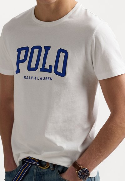Tricou alb din bumbac cu inscripția albastră "POLO". Design cu mâneci scurte și guler rotund. Purtați cu blugi din denim și un ceas la încheietura mâinii.