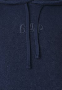 Felpa blu navy realizzata in tessuto misto cotone, dotata di tasca a marsupio e logo "GAP" ricamato. Include cordini e finitura testurizzata.