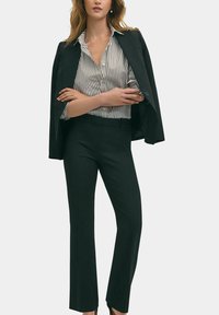 Černé ušité sako přes bílo-černě pruhovanou košili, spárované s černými rozšířenými kalhotami; hladká látka, čisté linie a žádné viditelné vzory.