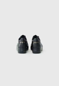 Baskets en cuir noir avec surface texturée, semelles en caoutchouc et logo doré au niveau du talon. Design minimaliste avec un profil bas.