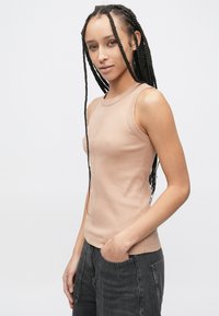 Beiges, geripptes Tanktop mit figurbetontem Schnitt, rundem Ausschnitt und ärmellosem Design, kombiniert mit dunkelgrauer Jeans.