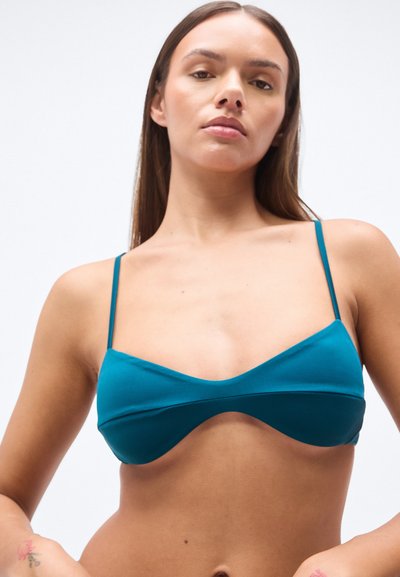 Τοπ μαγιό μπικίνι σε τιρκουάζ  χρώμα από ομαλό, ελαστικό ύφασμα. Διαθέτει λεπτές ρυθμιζόμενες τιράντες και μαλακές, καμπυλωτές ραφές, προσφέροντας έναν μινιμαλιστικό σχεδιασμό.