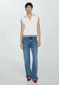 Sømløs hvid strik top med lynlåskrave, parret med lyseblå flared jeans. Skoene er røde med en spids tå design.