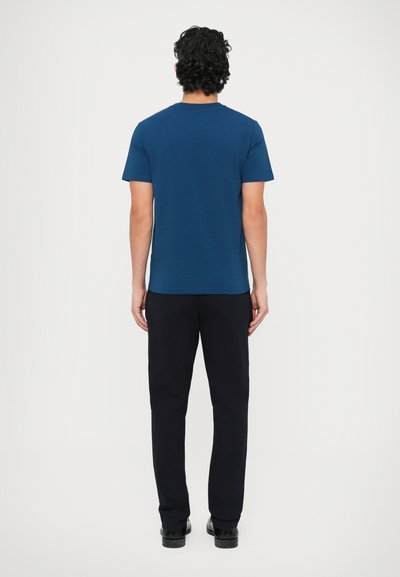 Námornícka modrá tričko s krátkym rukávom a okrúhlym výstrihom, v kombinácii s čiernymi nohavicami. Látka pôsobí hladko a strednej váhy.