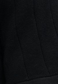 Μαύρο υφασμάτινο πλεκτό με εμφανή κάθετα ριγωτά μοτίβα και λεπτές υφαντές λεπτομέρειες.