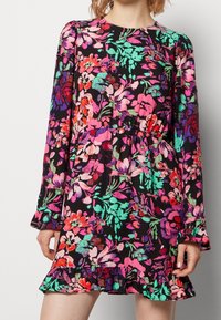 Vestido floral en negro, con vibrantes flores rosas, verdes y rojas. Mangas largas con puños rizados y un dobladillo acampanado.