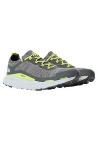 Zapatillas deportivas grises con parte superior de punto, acentos reflectantes y cordones amarillos brillantes. Suela blanca gruesa con suela exterior de goma negra para tracción.