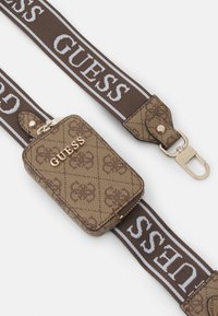 Pochette marron à motifs avec le logo "GUESS" doré ; comprend une sangle complémentaire avec le texte "GUESS" en blanc, un fermoir en métal et un détail de fermeture éclair.