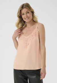 Peedi satinist kampsun, millel on pitsdetailid krae ääres, õhukesed reguleeritavad rihmad ja lõdvestunud sobivus, kokku sobitatud mustade nahkpükstega.