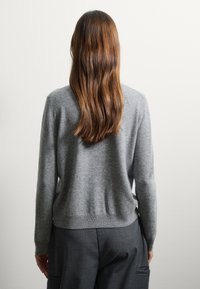 Pull en tricot gris à manches longues, col rond et ourlet côtelé, associé à un pantalon gris foncé. Il a l'air doux et confortable.