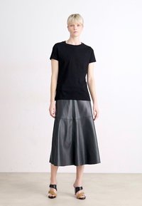 Melnas īsām piedurknēm T-kreklas, apvienots ar garu, augsta jostasvietas, krokām veidotu melnu ādas svārku. Modelis stāv uz neitrāla fona.