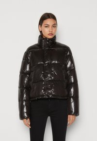 Chaqueta de plumas negra con acabado brillante, cuello alto, botones a presión y diseño corto. Presenta secciones acolchadas y mangas amplias.